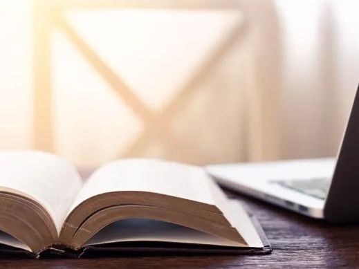 An open Bible beside a laptop